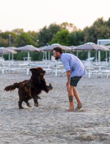 Uomo gioca felice con cane sulla spiaggia deserta al tramonto.