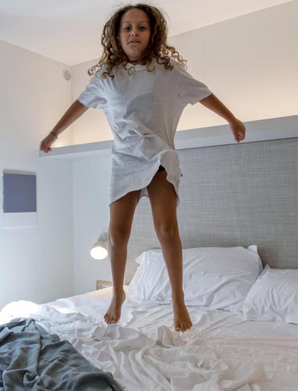 Bambina felice salta sul letto in una stanza luminosa e accogliente.