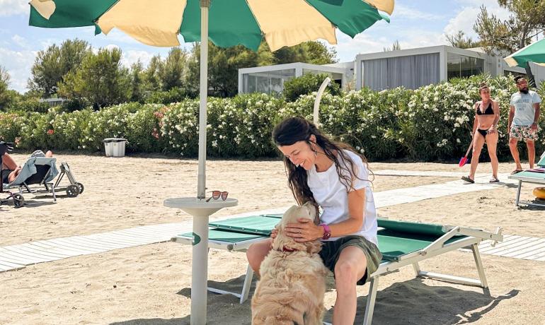 Donna coccola cane sotto ombrellone in spiaggia, atmosfera serena e rilassata.