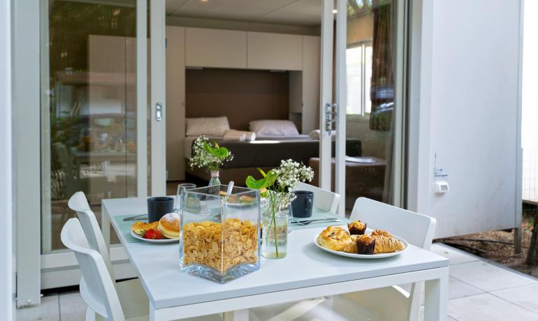 Frühstück im Freien mit Gebäck, Müsli und Blumen vor einem gemütlichen Zimmer.