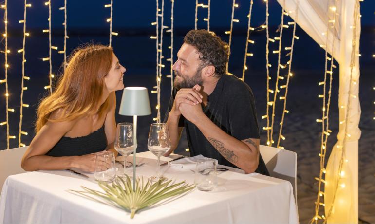 Romantisches Abendessen am Strand mit sanften Lichtern, glückliches und lächelndes Paar.