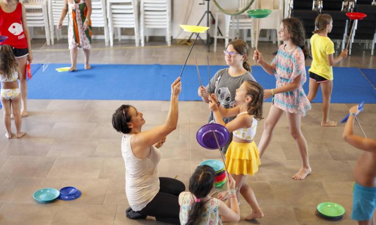 Begeisterte Kinder lernen, mit drehenden Tellern zu jonglieren, angeleitet von einer lächelnden Lehrerin.