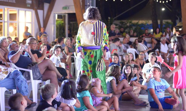Begeisterte Menge beobachtet bunten Clown, Kinder lächeln und klatschen.