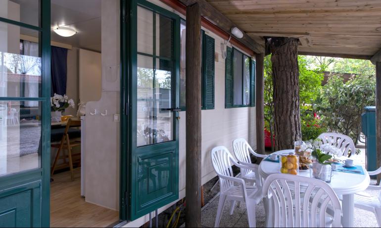 Gemütliche Veranda mit gedecktem Tisch, umgeben von üppiger Natur.