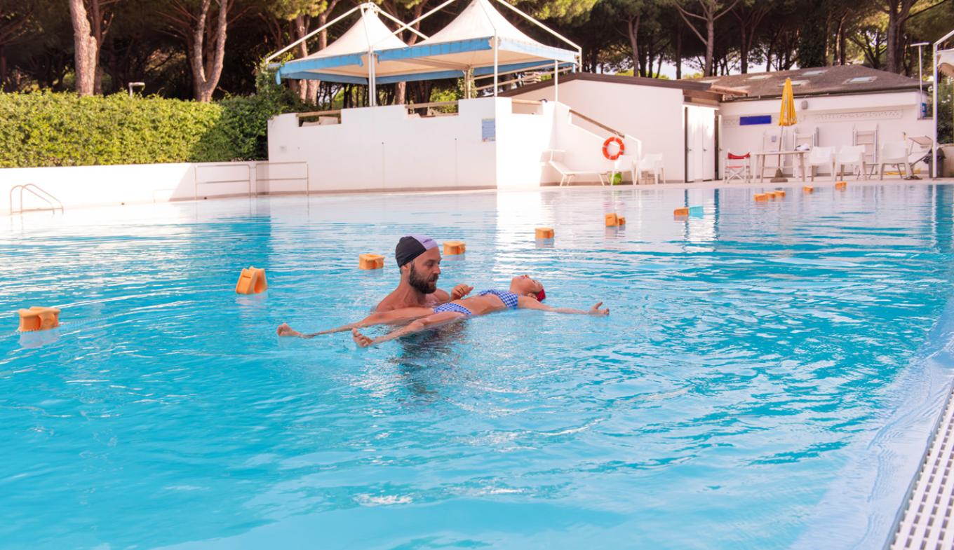 Istruttore aiuta bambino a galleggiare in piscina, atmosfera serena e sicura.