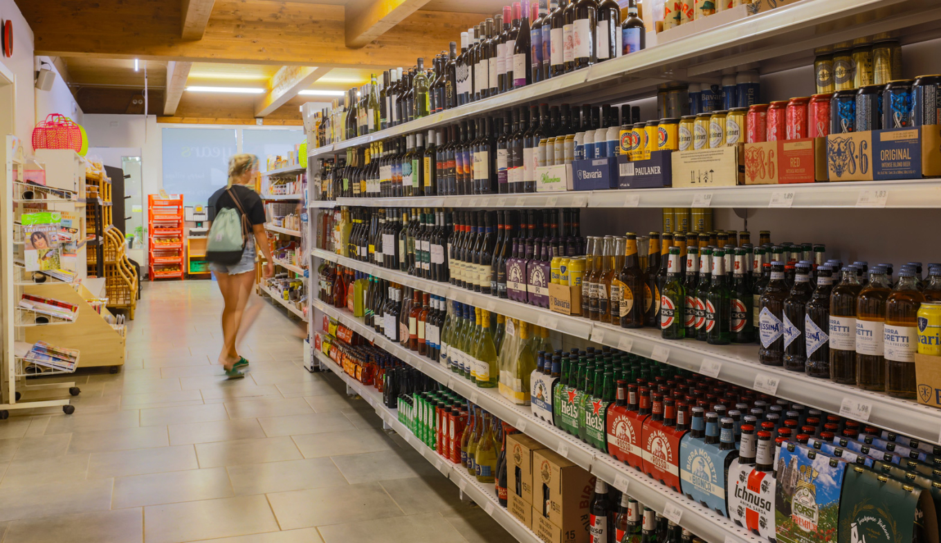 Supermercato accogliente, scaffali pieni di vini e birre, cliente passeggia tra le corsie.