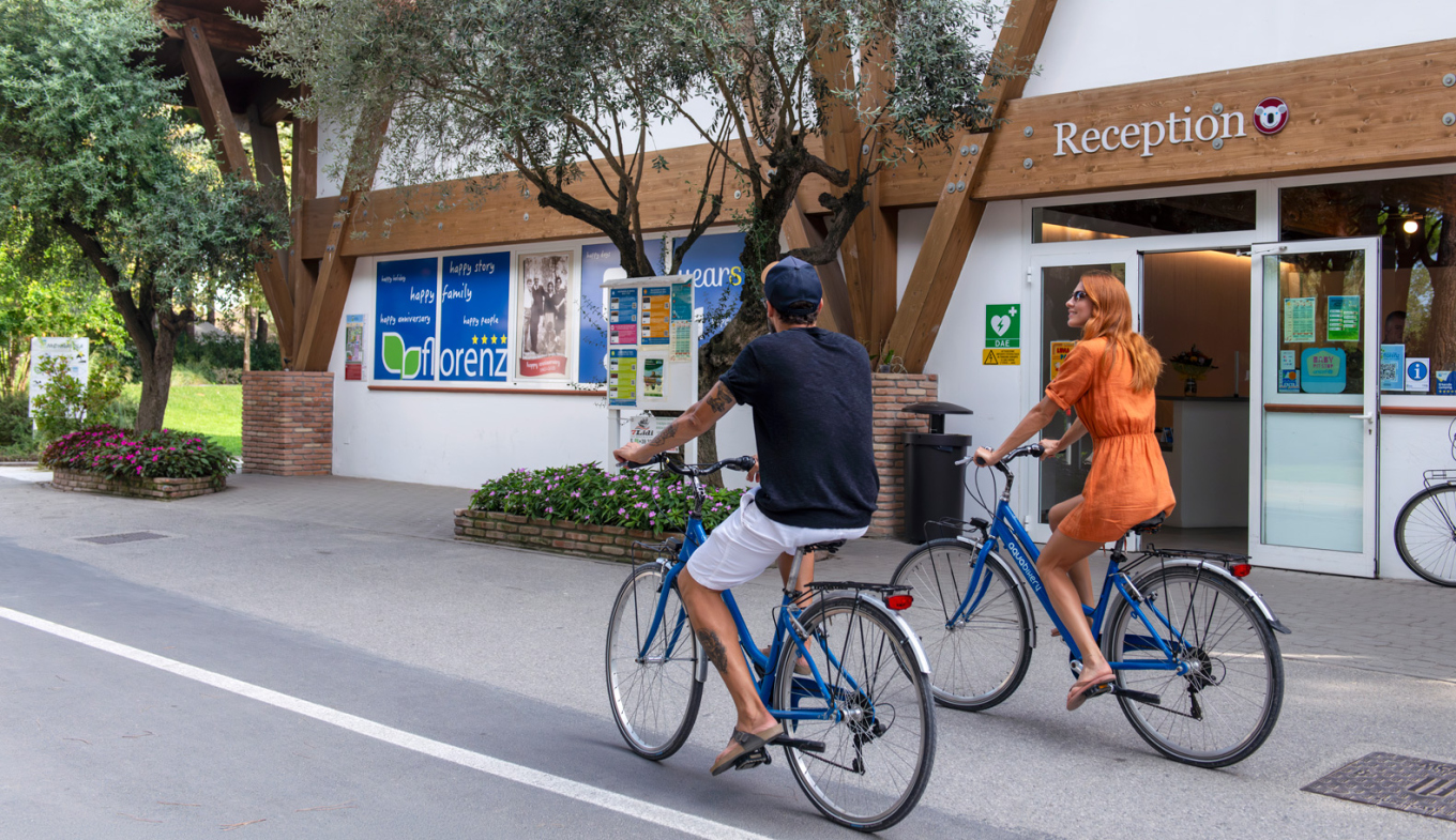 Coppia felice in bicicletta, atmosfera estiva e accogliente davanti a una reception.