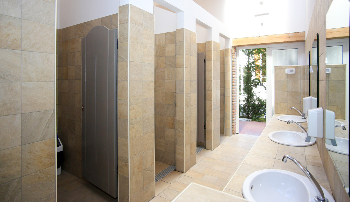 Bagno pubblico moderno, pulito e luminoso, con lavandini bianchi e cabine doccia beige.