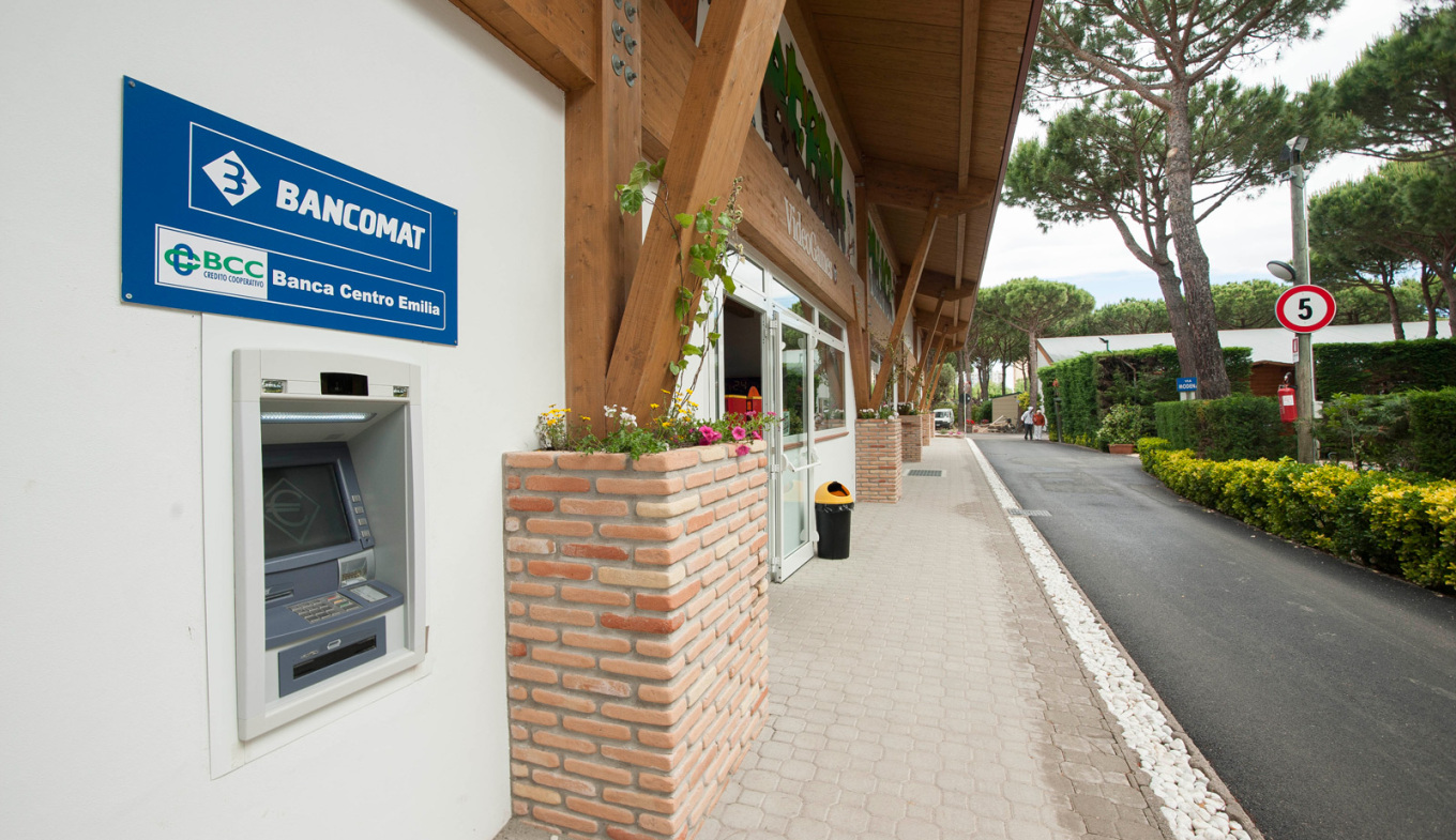 Bancomat all'aperto, atmosfera serena con alberi, fiori e un vialetto tranquillo.