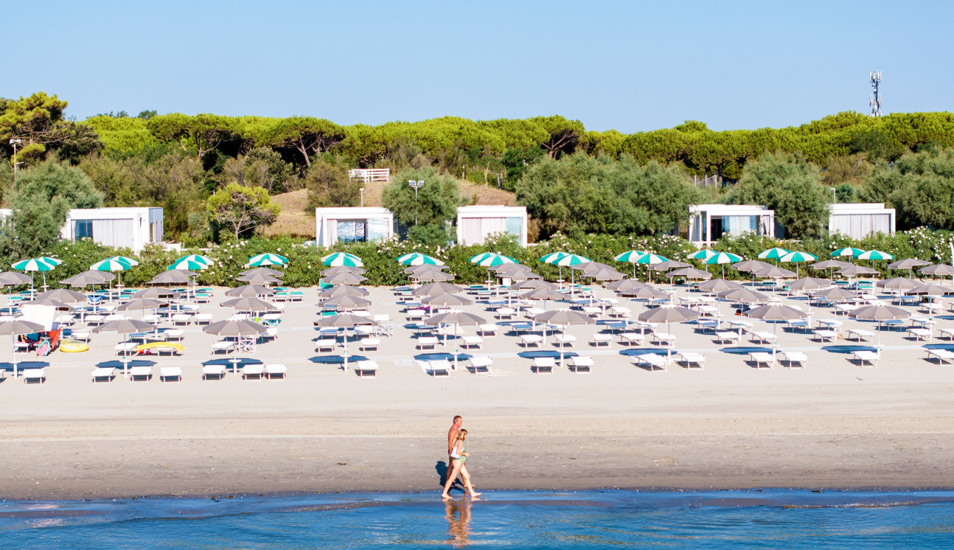 Spiaggia tranquilla, ombrelloni colorati, mare calmo, due persone camminano sulla riva.