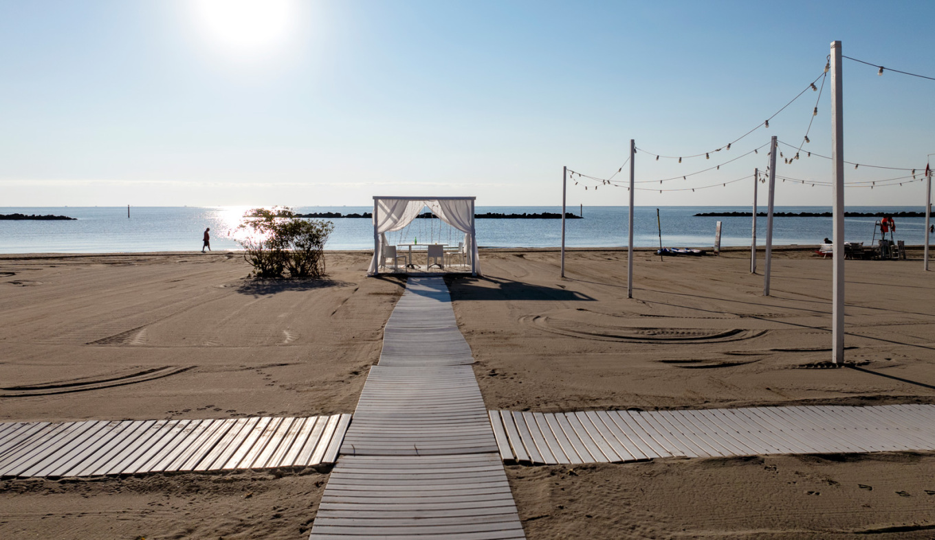Spiaggia tranquilla al tramonto, con gazebo bianco e luci sospese, atmosfera romantica.