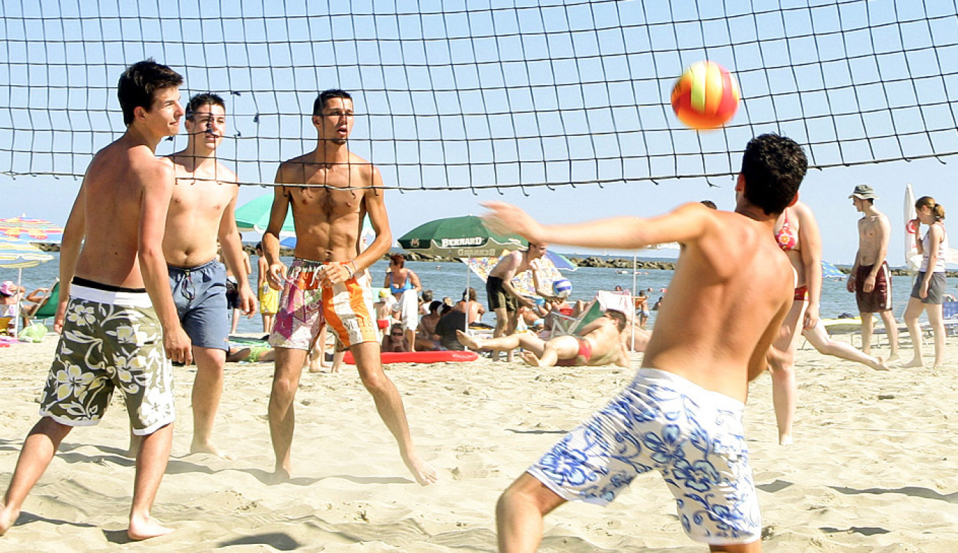 Giovani giocano a beach volley, sole splendente, sabbia dorata, energia e divertimento estivo.