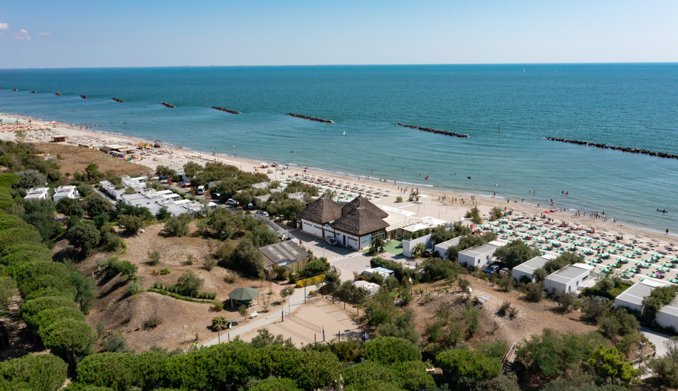 Spiaggia soleggiata, mare calmo, ombrelloni colorati, natura rigogliosa, atmosfera rilassante e gioiosa.