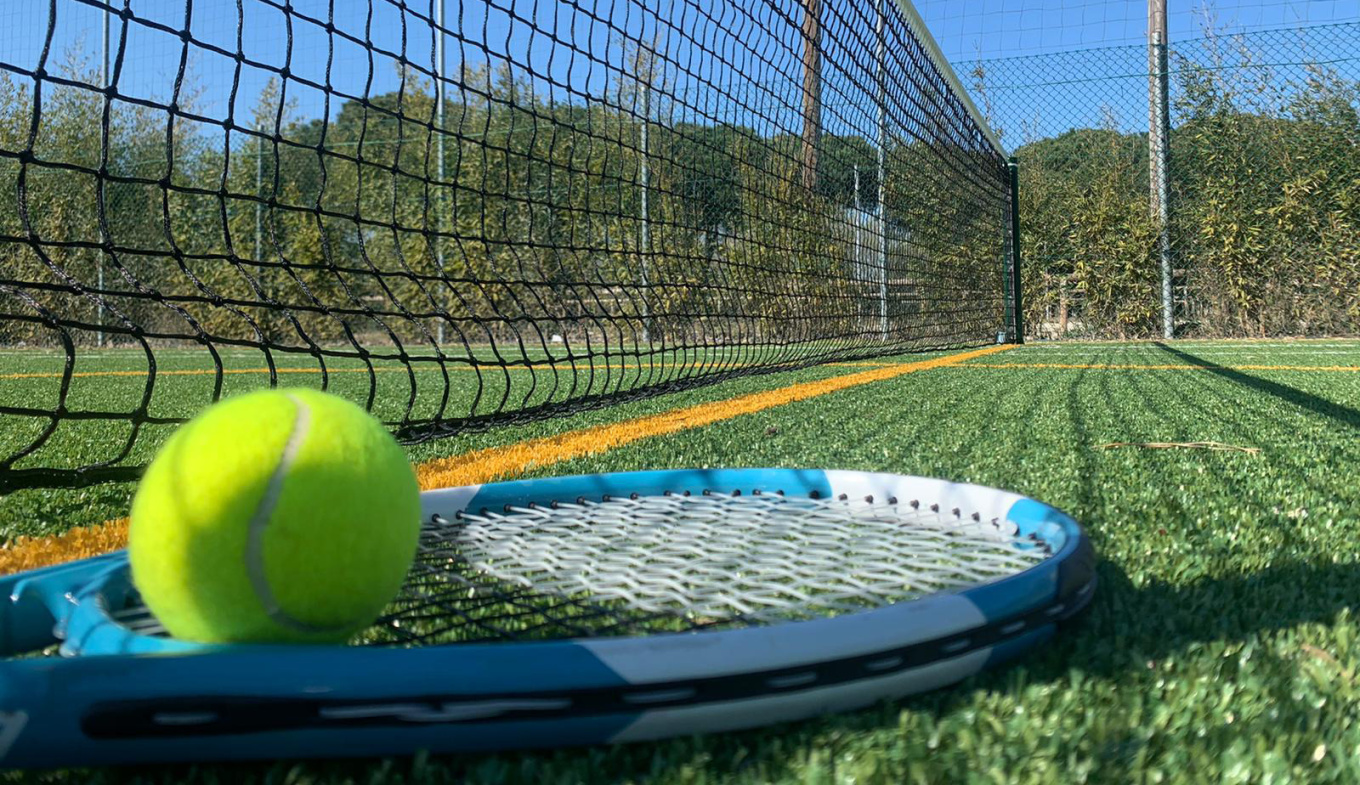 Racchetta e pallina da tennis su campo verde, sole splendente, atmosfera di gioco e libertà.