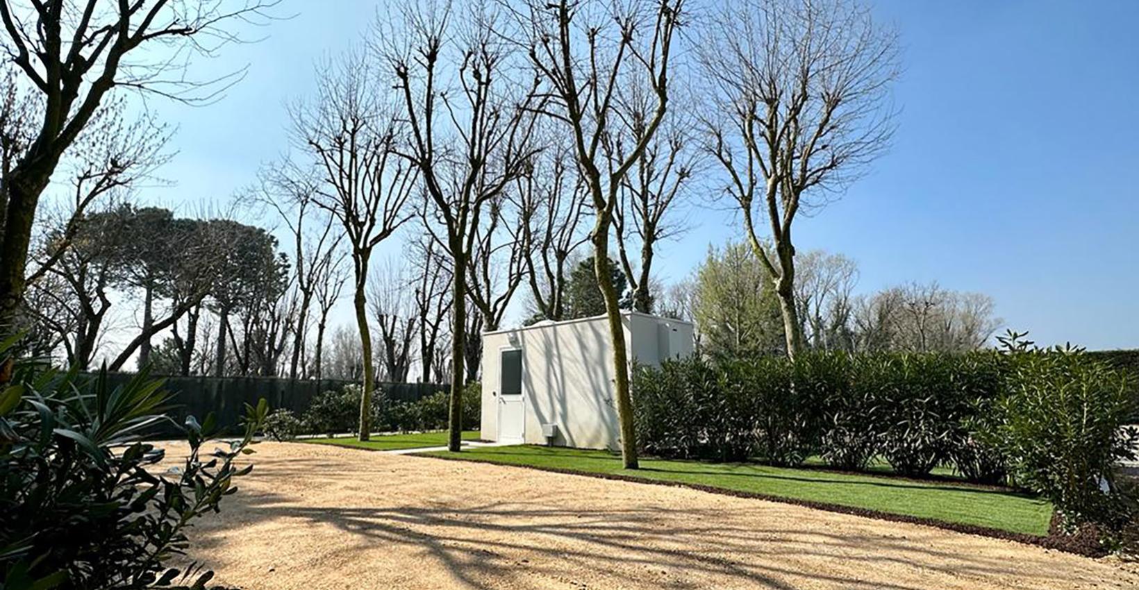 Giardino sereno con alberi spogli, cielo azzurro e casetta bianca immersa nella natura.