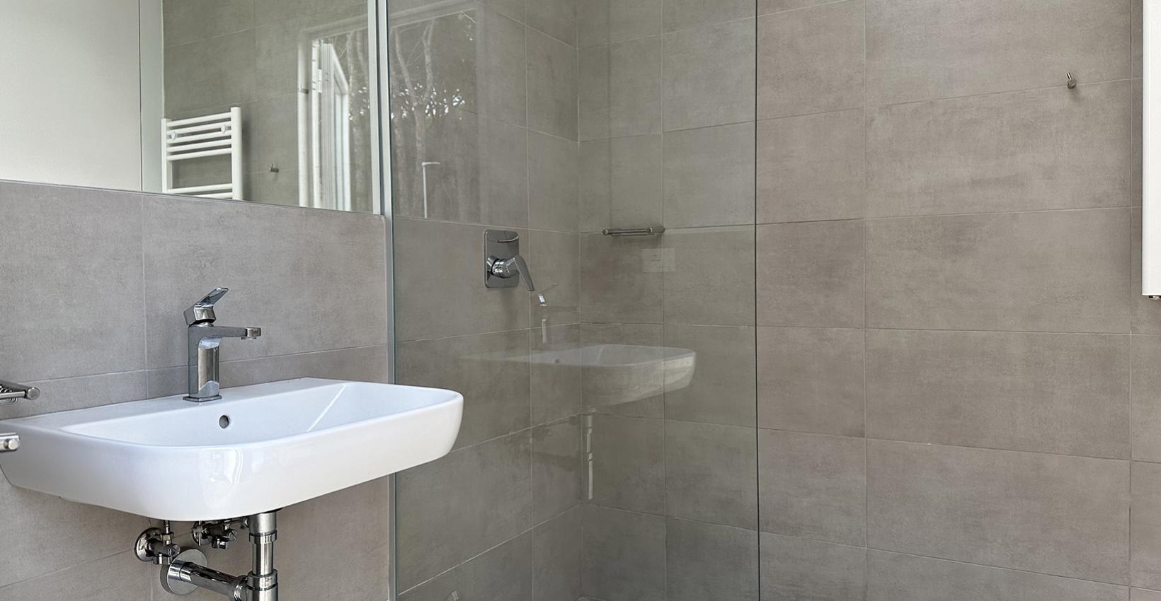 Bagno moderno, minimalista, con doccia a pioggia e lavabo sospeso, atmosfera elegante e luminosa.
