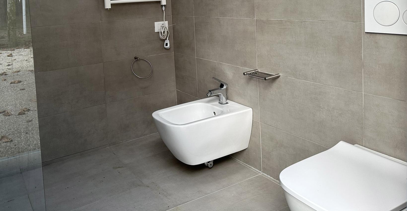 Bagno moderno, minimalista, con bidet e wc bianchi su piastrelle grigie, atmosfera serena.
