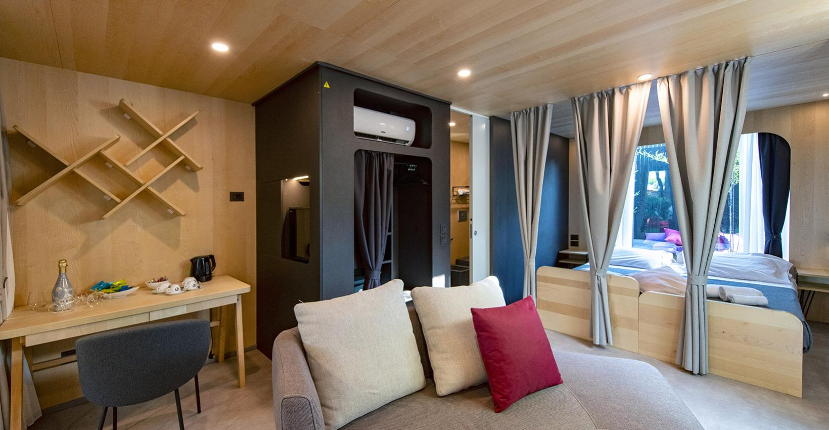 Accogliente monolocale in legno, moderno e luminoso, con angolo relax e letto separato da tende.