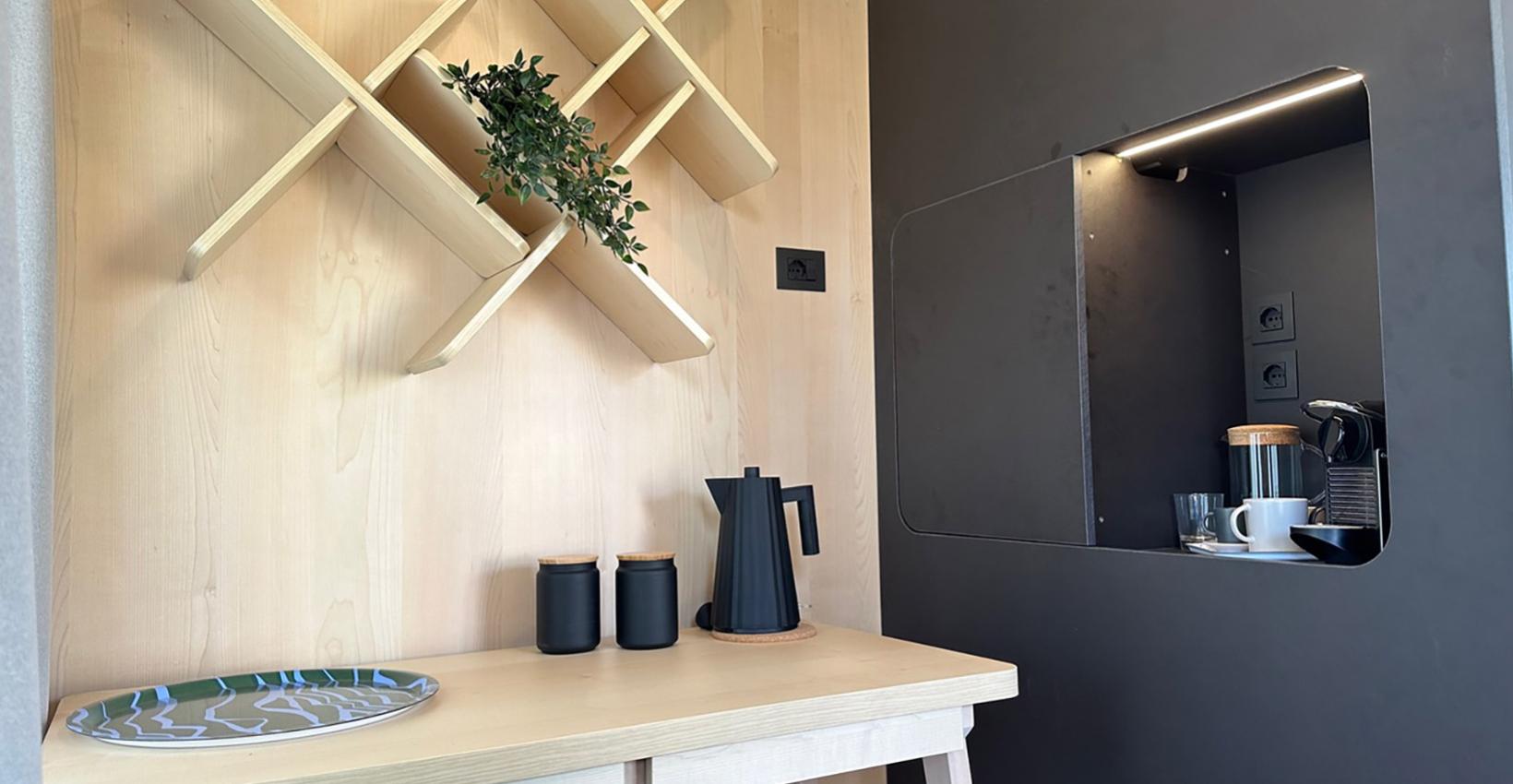 Interno minimalista con scaffale geometrico, piante, macchina da caffè e dettagli moderni, caldi e accoglienti.