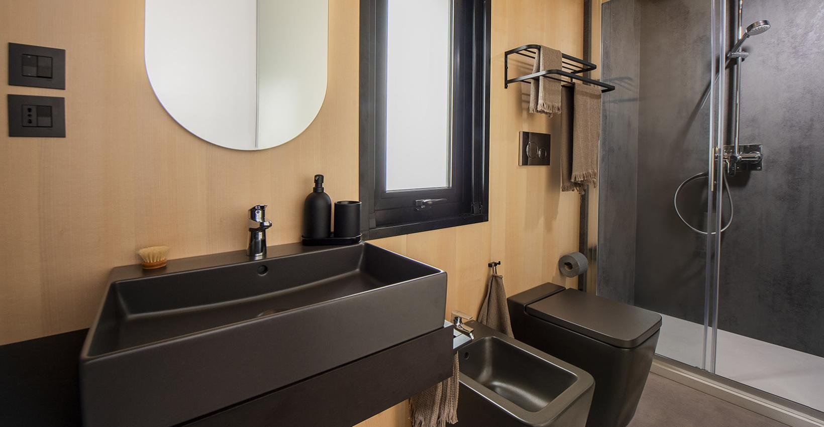 Bagno moderno elegante, colori scuri, legno chiaro, doccia spaziosa, atmosfera rilassante e sofisticata.