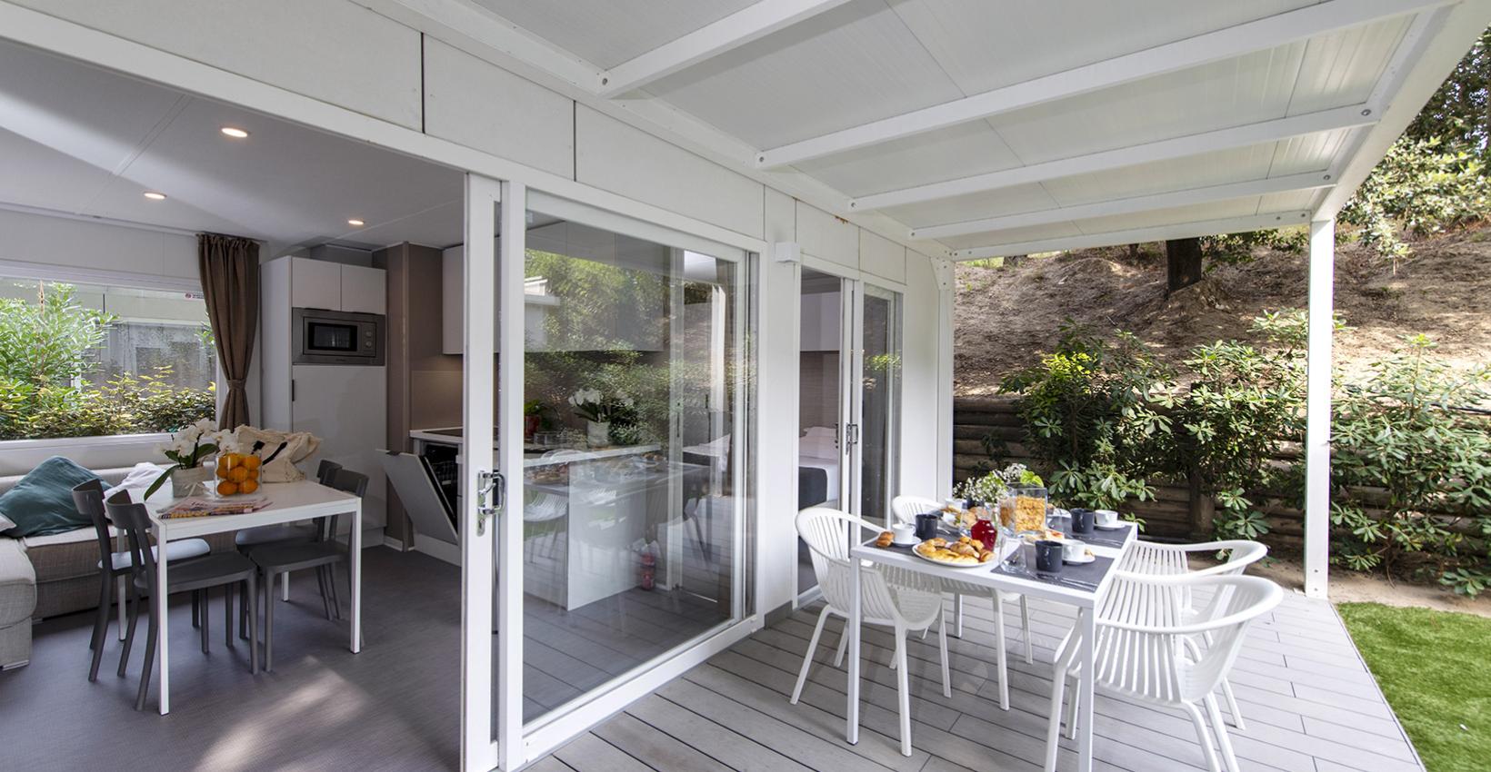 Terrazza luminosa con tavolo apparecchiato, vista su giardino verde, atmosfera accogliente e rilassante.