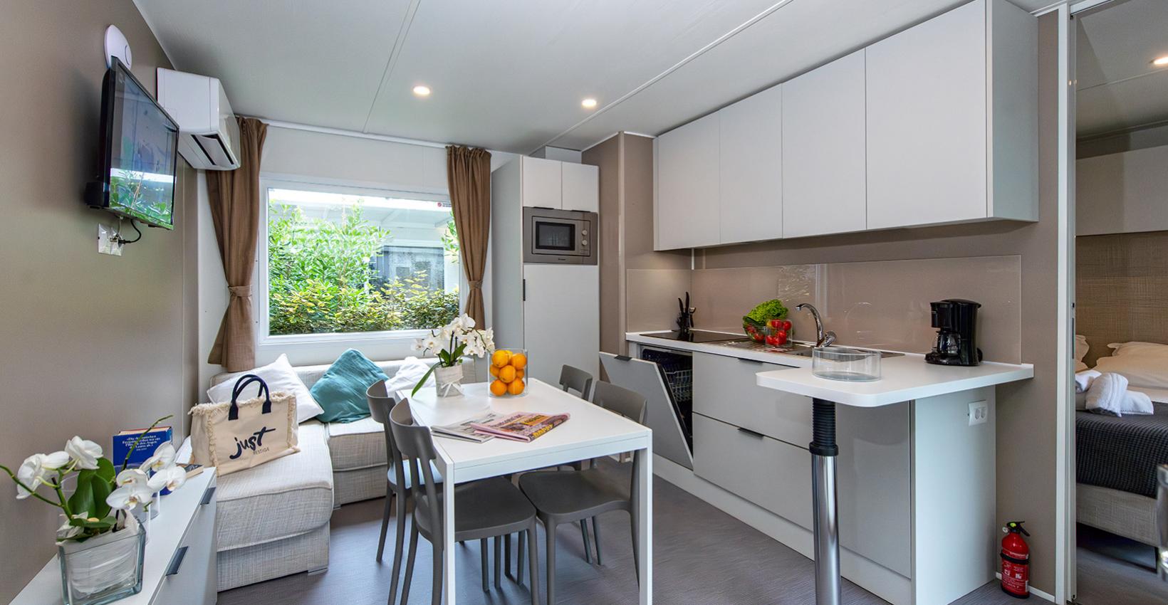 Cucina moderna e luminosa, tavolo bianco, fiori, arance e vista verde rilassante.