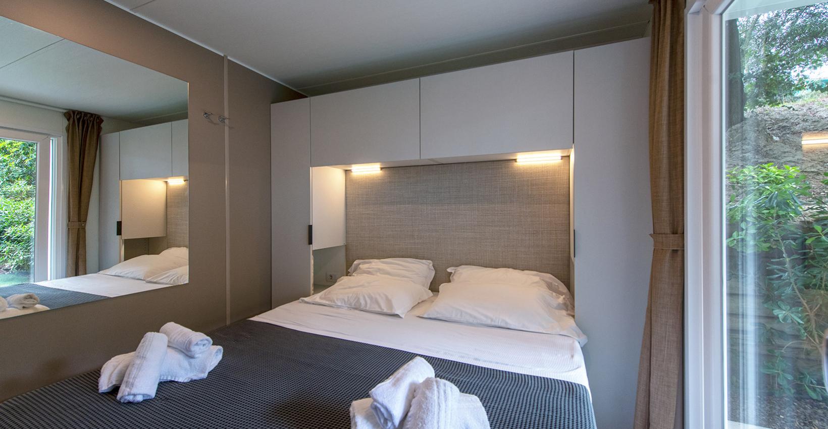 Camera accogliente e moderna, letto matrimoniale con luci soffuse e asciugamani piegati.