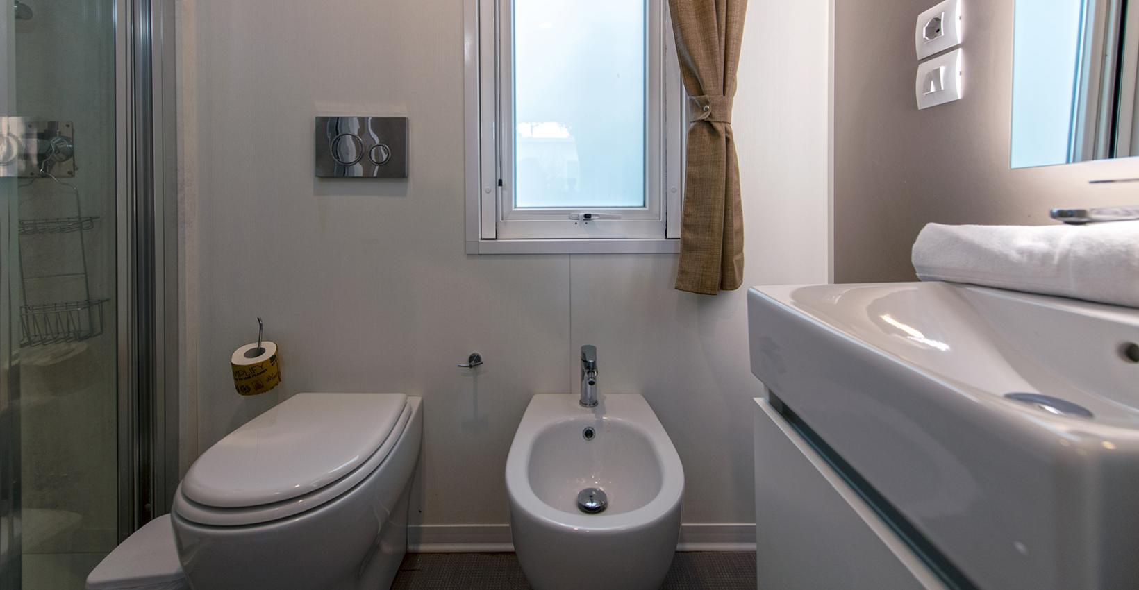 Bagno moderno, compatto, con finestra, tenda marrone, doccia, bidet e lavandino elegante.