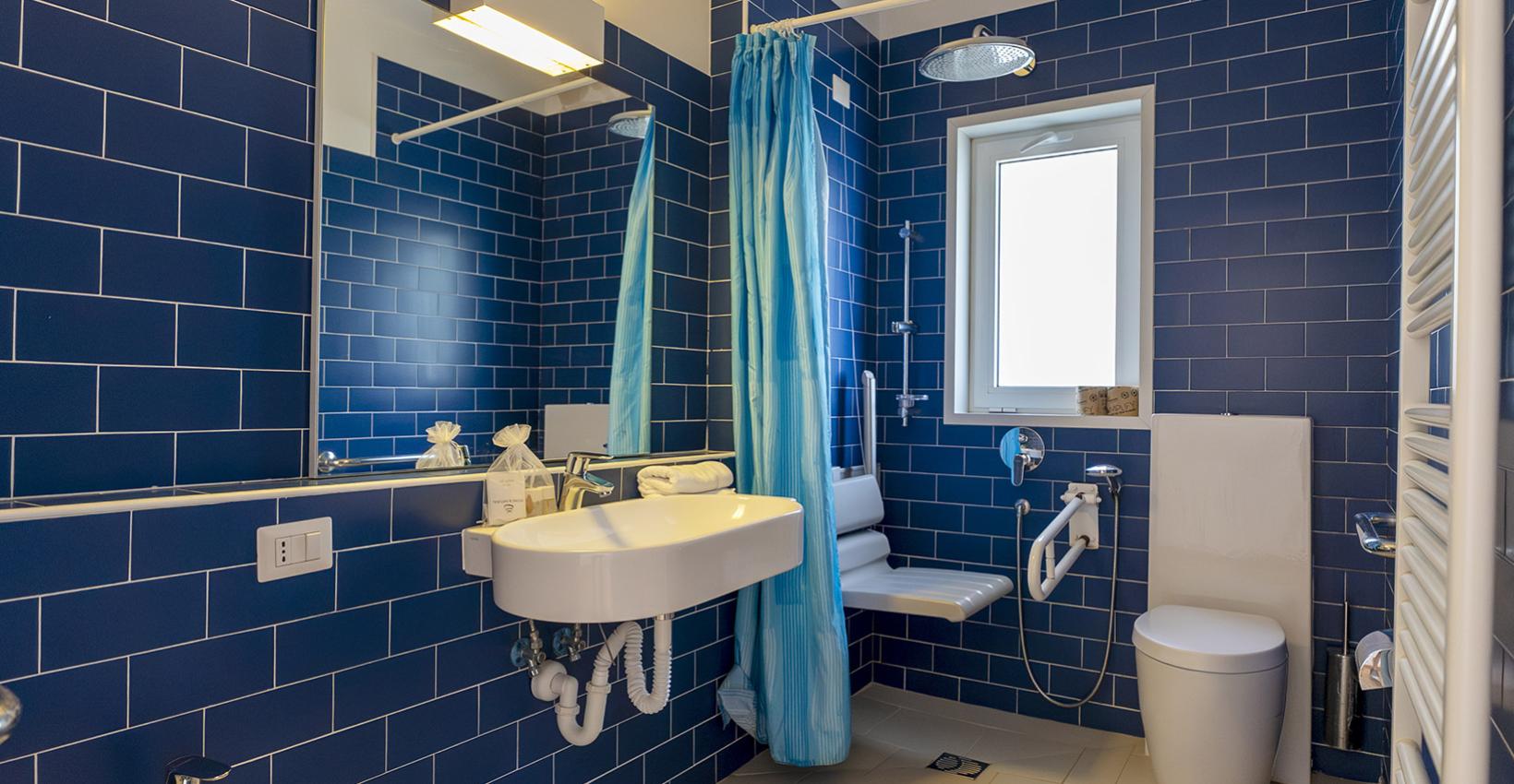 Bagno moderno con piastrelle blu, doccia, lavabo e servizi accessibili, atmosfera luminosa e accogliente.