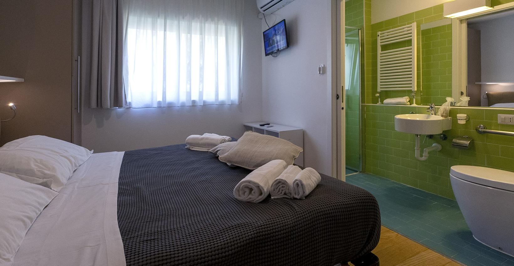 Camera accogliente, letto ordinato, bagno verde vivace, atmosfera rilassante e moderna.