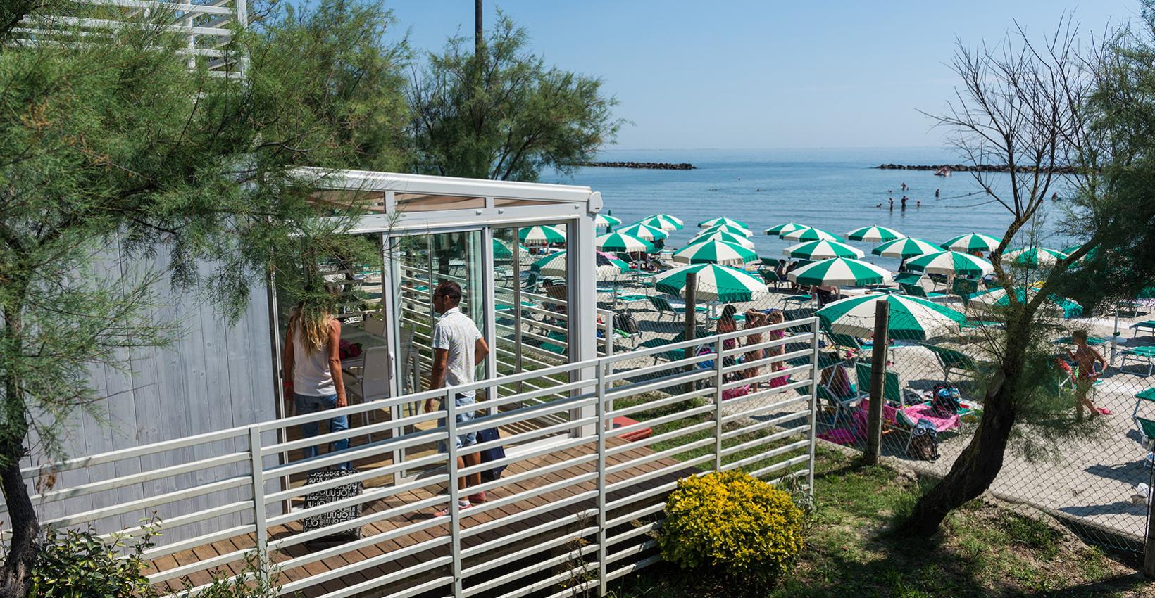 Spiaggia soleggiata, ombrelloni verdi, mare calmo, atmosfera rilassante, persone godono il panorama estivo.