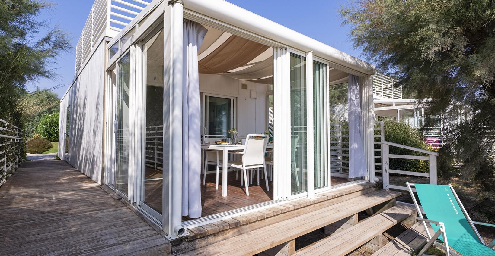 Moderna veranda bianca con tende, immersa nel verde, perfetta per relax estivo.