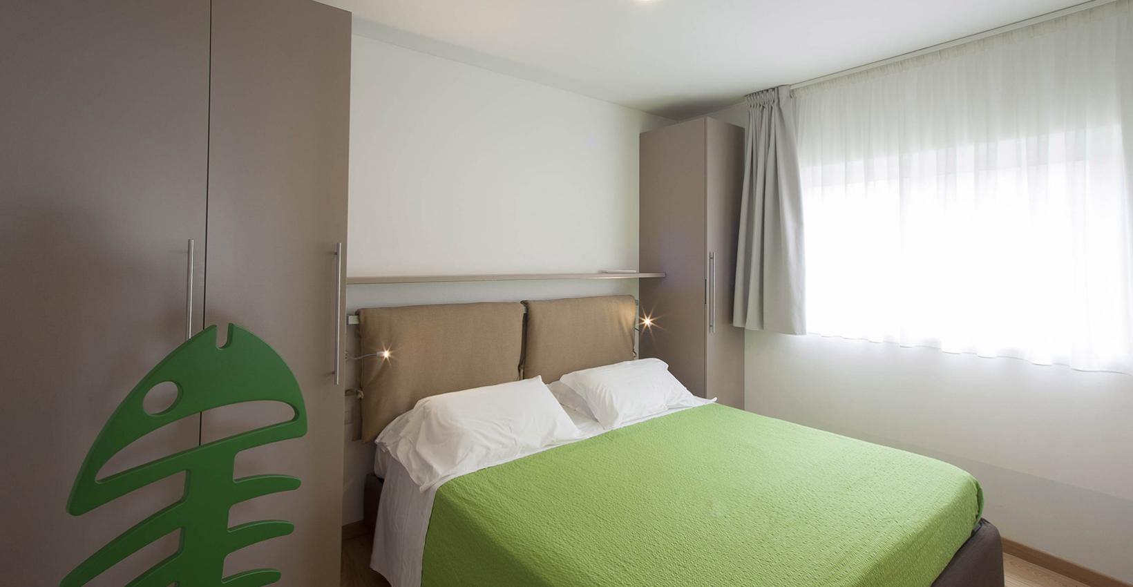 Camera luminosa, letto verde, armadi moderni, atmosfera serena e accogliente.