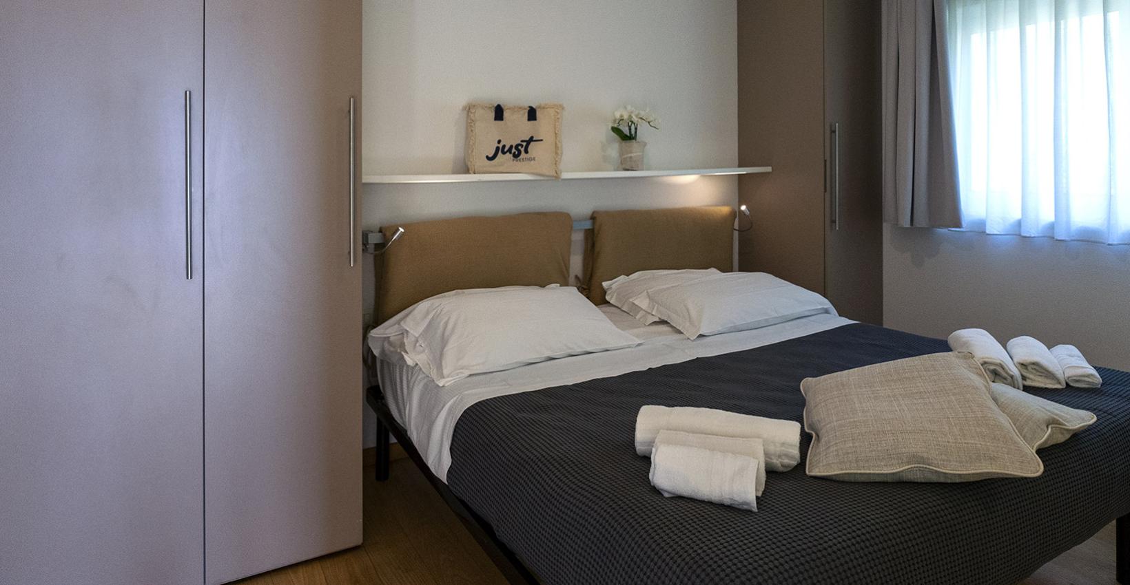 Camera accogliente e ordinata, letto matrimoniale con cuscini e asciugamani, luce soffusa.