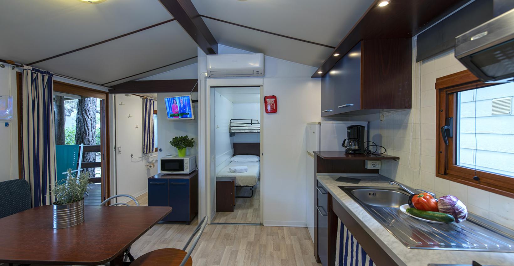 Accogliente casa mobile con cucina, tavolo, TV, e vista su un bosco luminoso.