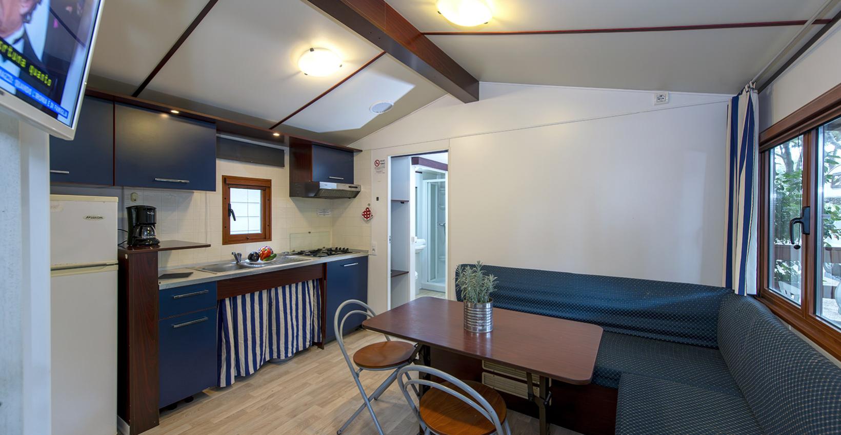 Cucina accogliente con mobili blu, tavolo in legno e luce calda, atmosfera rilassante.