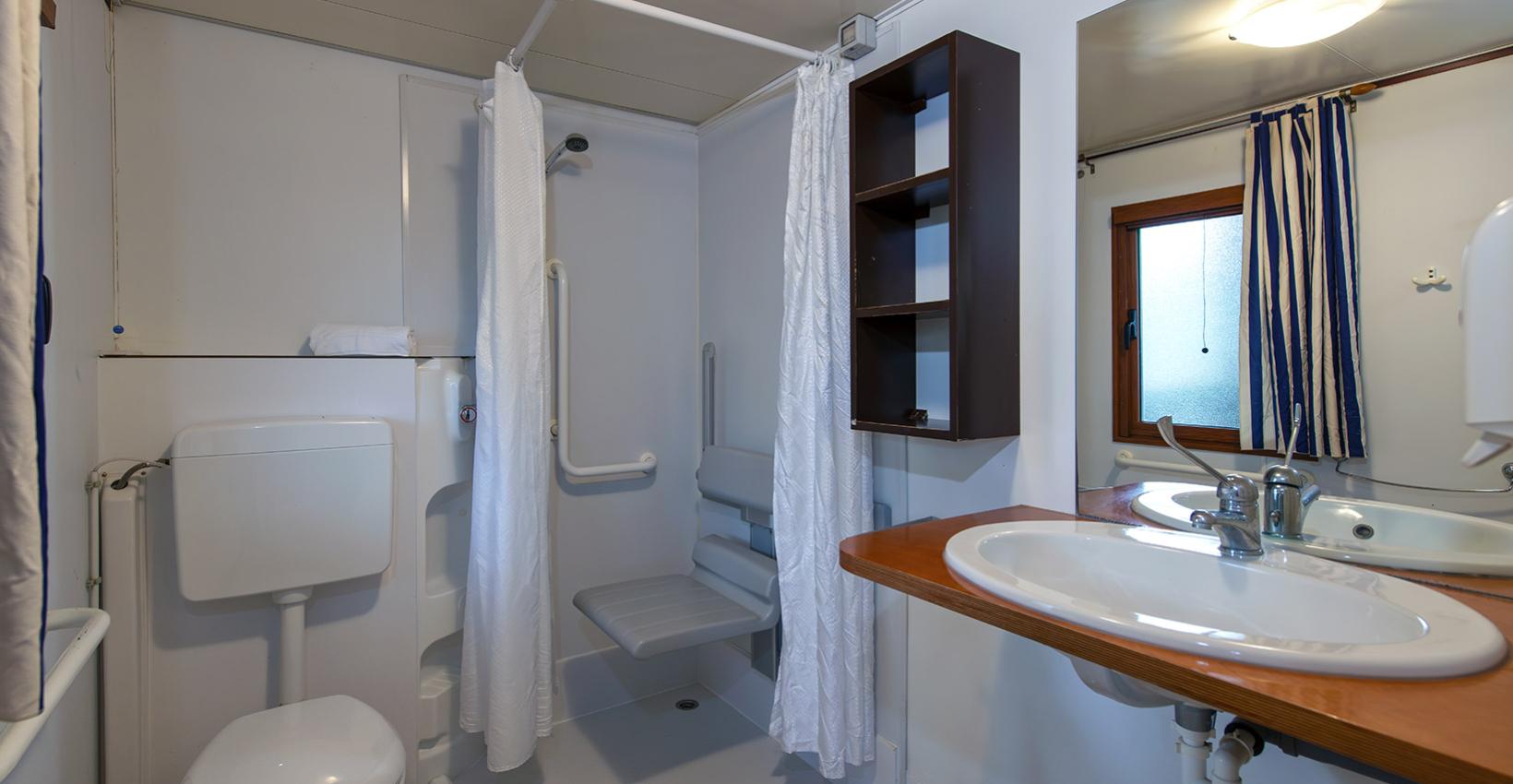 Bagno accessibile, doccia con sedile e maniglie, ambiente chiaro e ordinato.