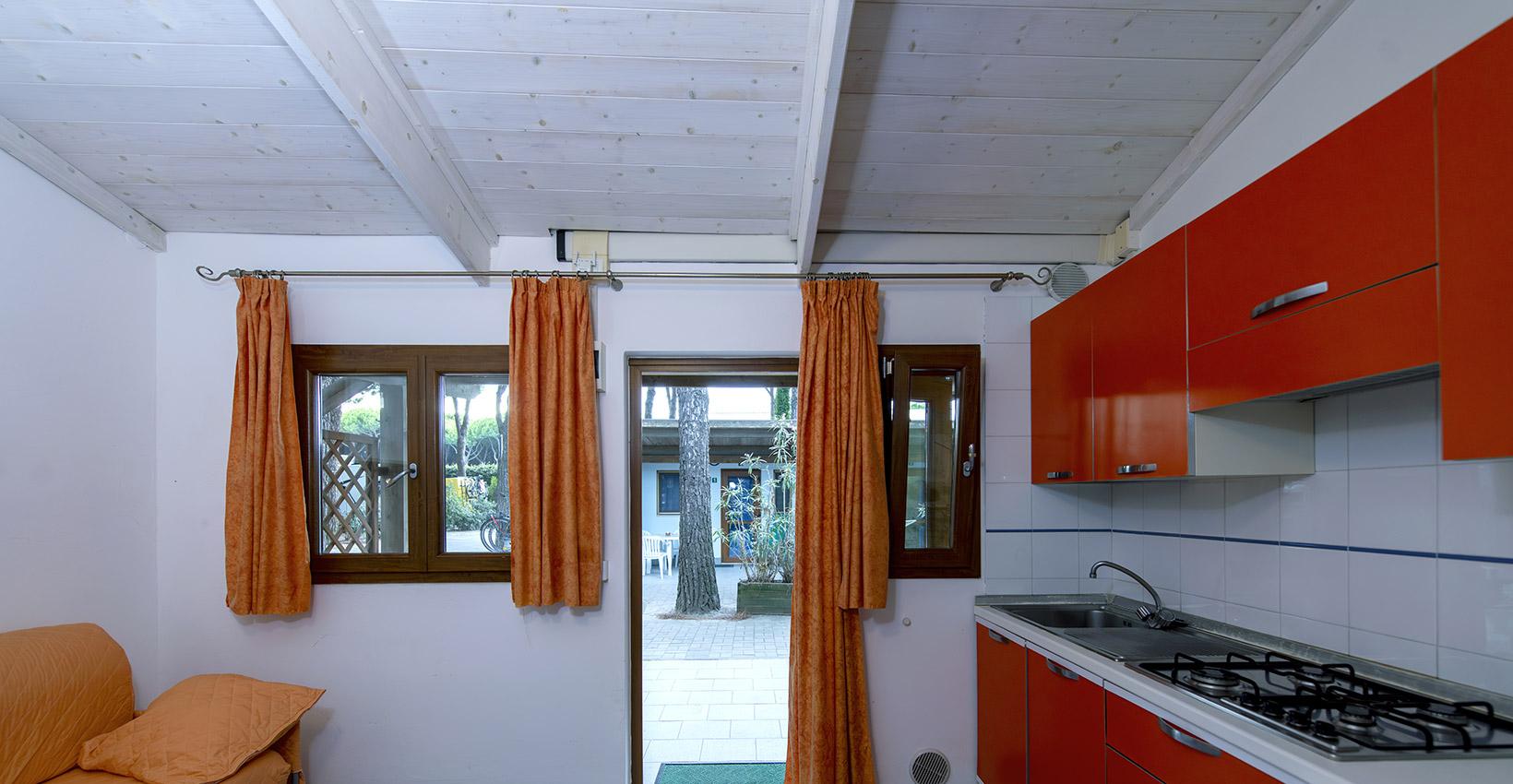 Cucina luminosa, arredi arancioni, vista su giardino verde, atmosfera accogliente e rilassante.