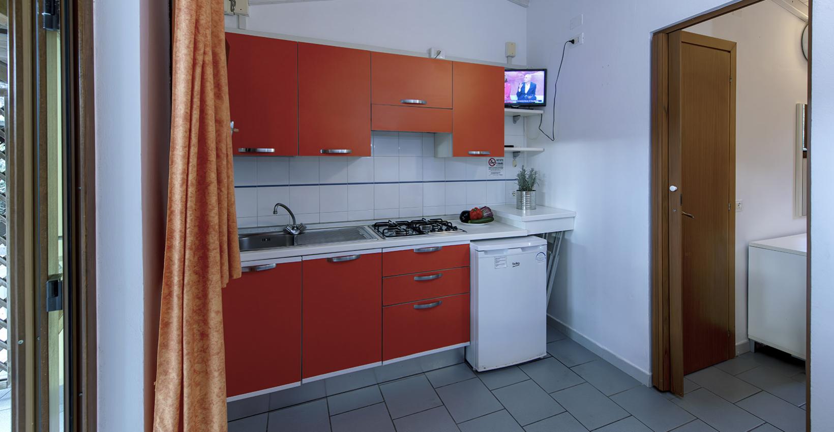 Cucina accogliente con mobili rossi, piccola TV, atmosfera calda e familiare.