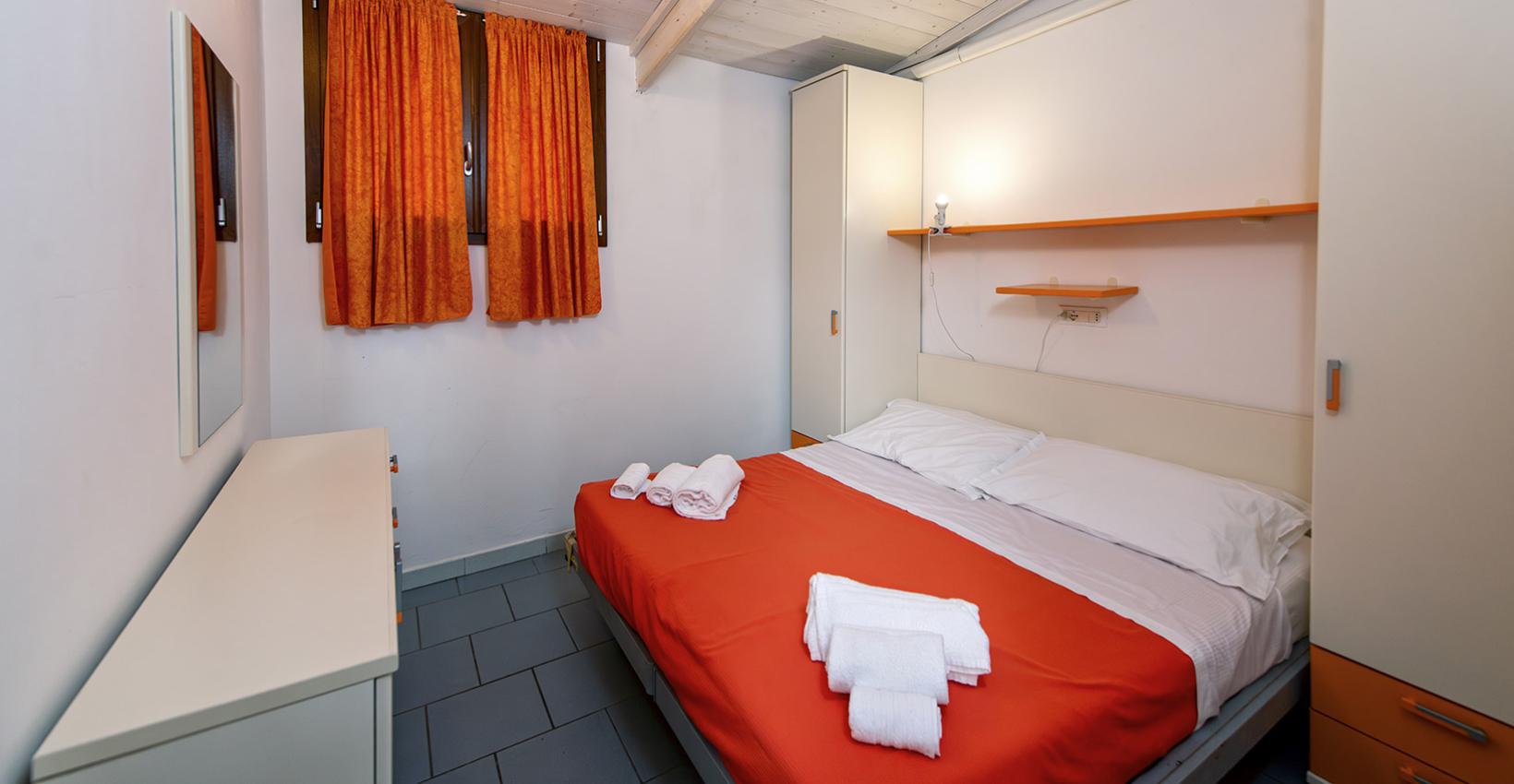 Camera accogliente, letto arancione, tende abbinate, atmosfera calda e luminosa.
