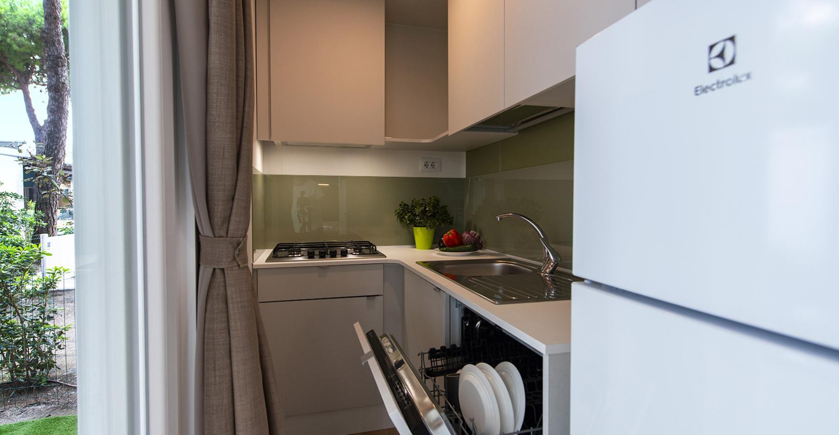 Cucina moderna luminosa, compatta, con lavastoviglie aperta e vista su giardino verde.