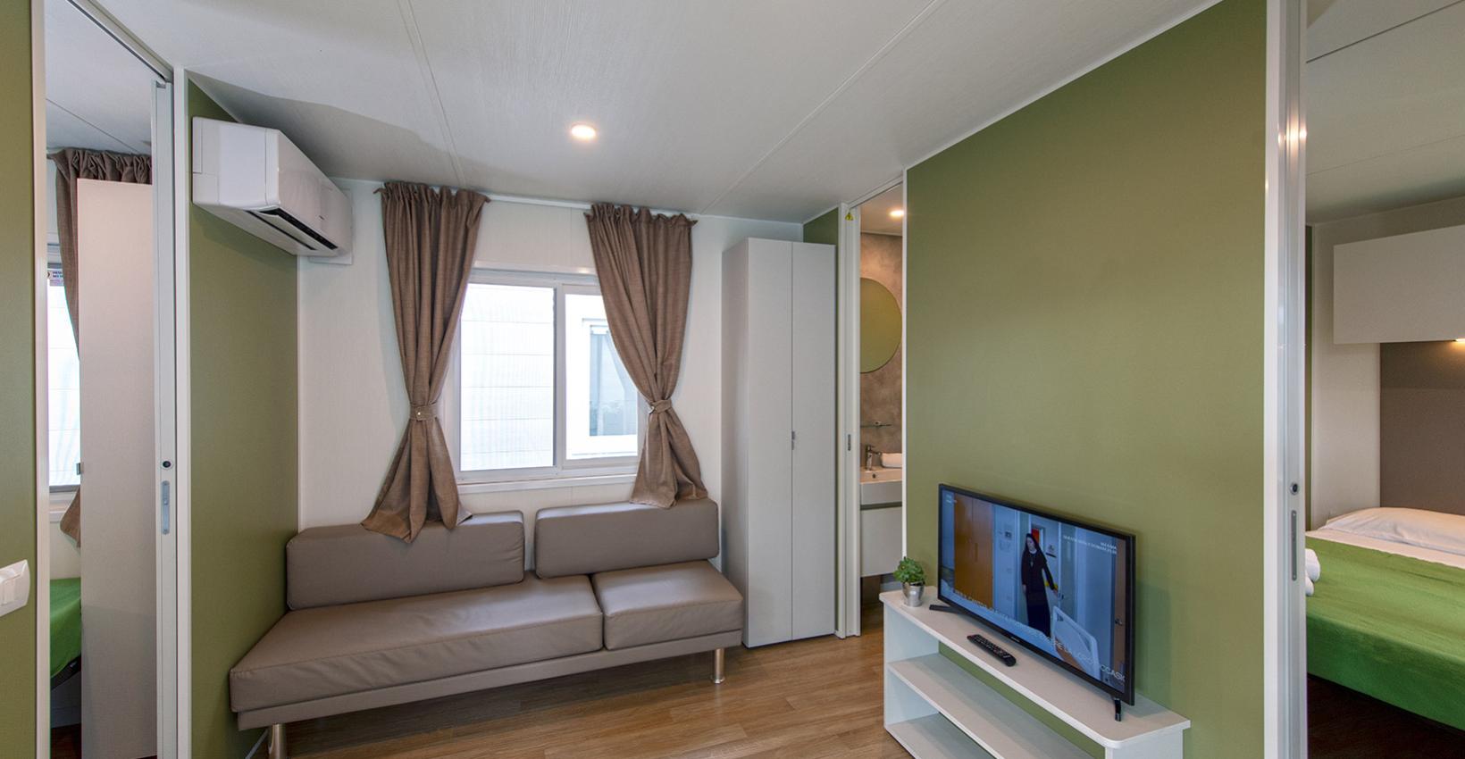 Moderno soggiorno con divano grigio, TV e pareti verde oliva, accogliente e luminoso.