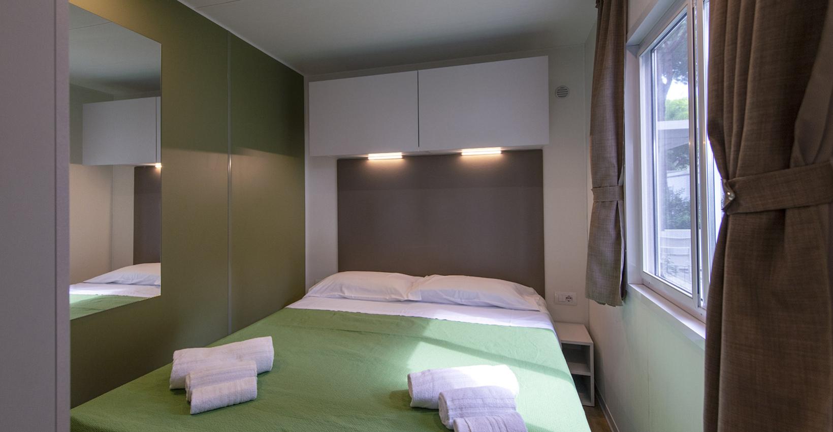 Camera accogliente con letto matrimoniale, pareti verdi, luce soffusa e teli bianchi piegati.