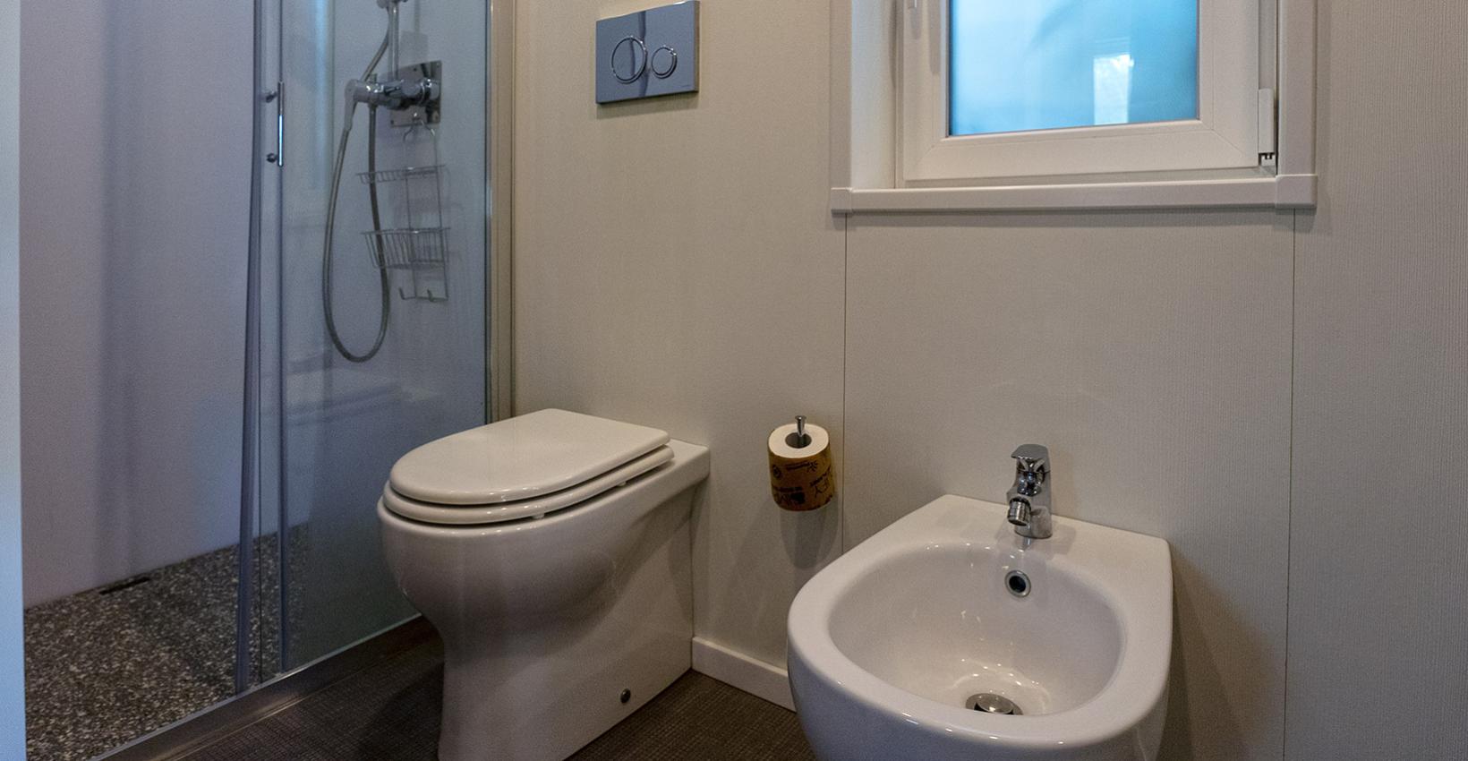 Bagno moderno con doccia, WC e bidet, illuminato da luce naturale attraverso una finestra.