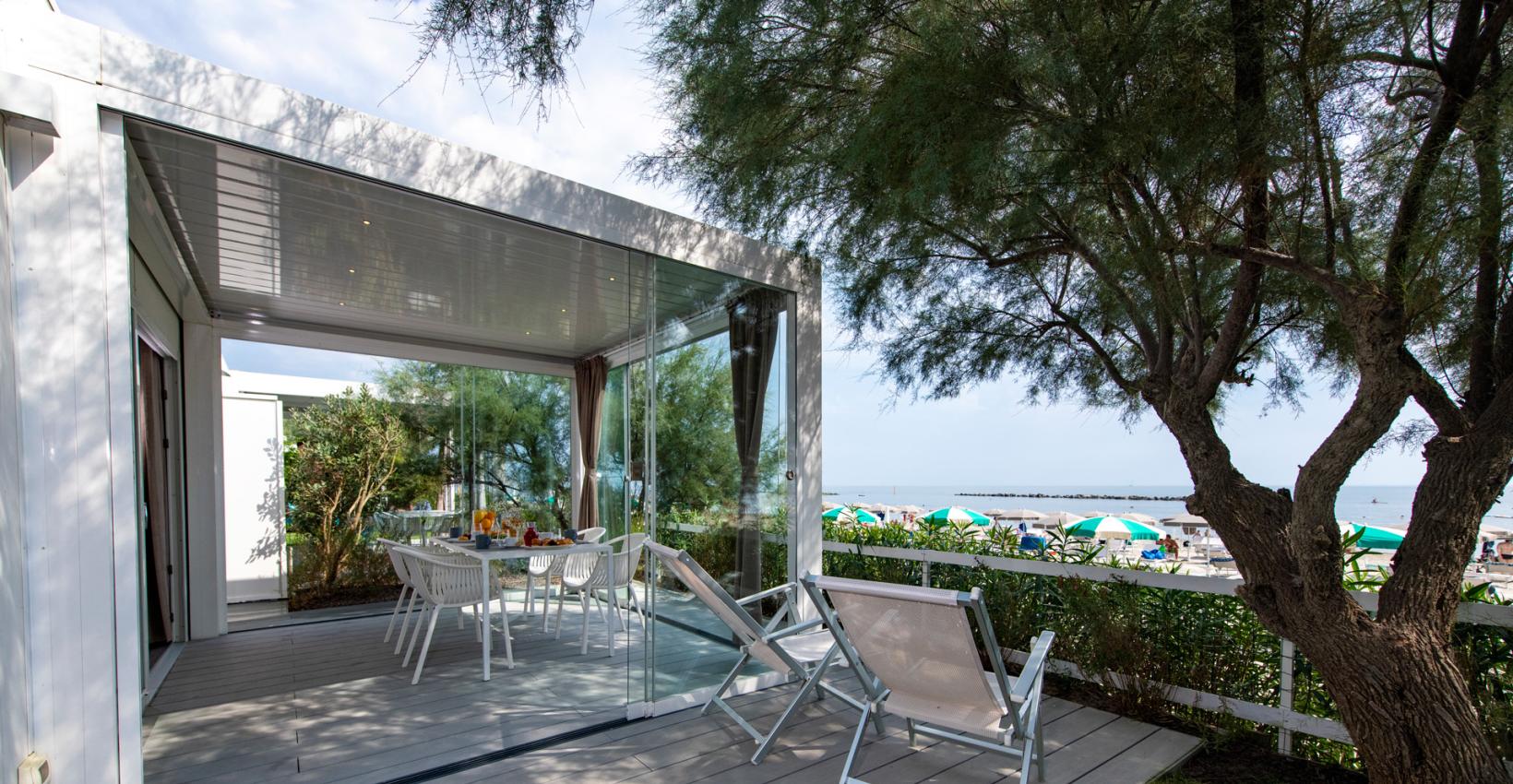 Terrazza moderna vista mare, sedie bianche, ombrelloni colorati, atmosfera rilassante e naturale.