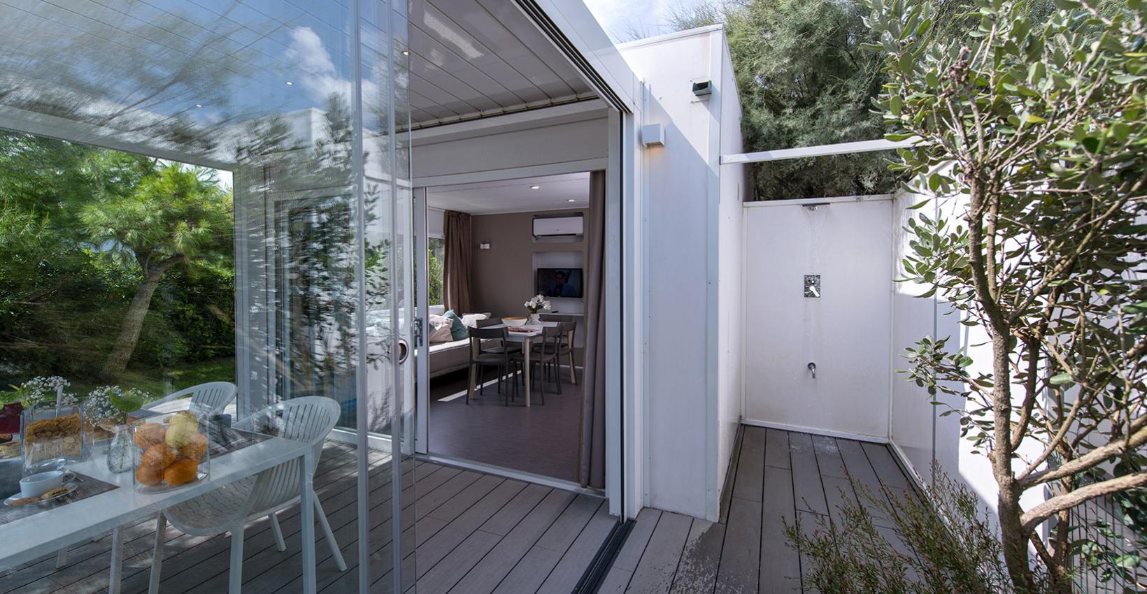 Elegante veranda moderna con tavolo apparecchiato, immersa nel verde, trasmette serenità e freschezza.