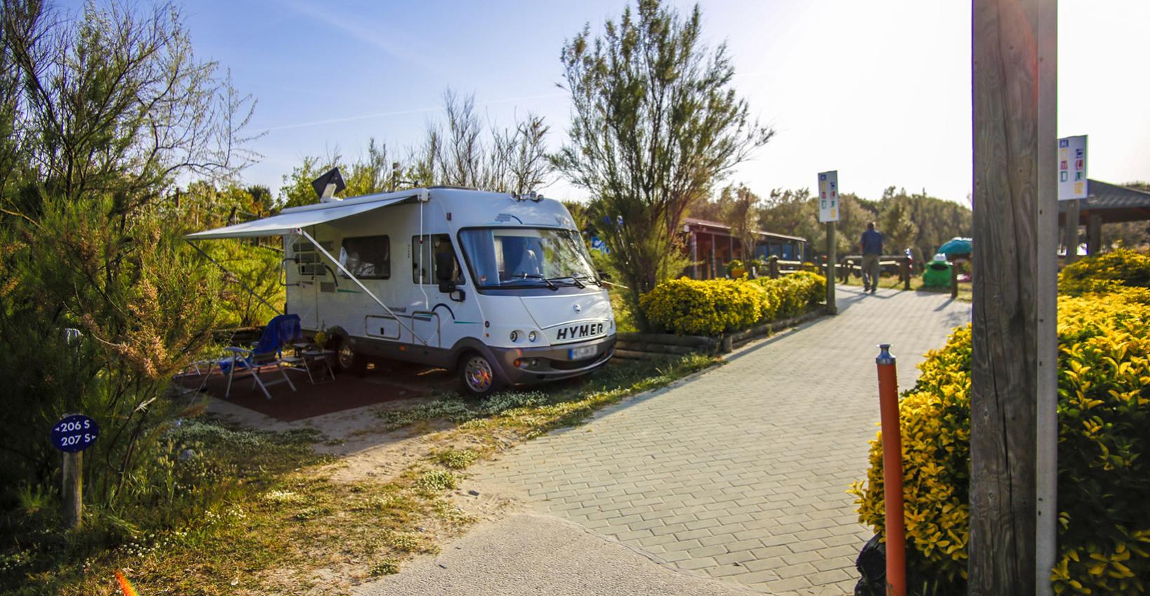 Camper in campeggio soleggiato, sedie all'aperto, atmosfera rilassante tra natura e tranquillità.