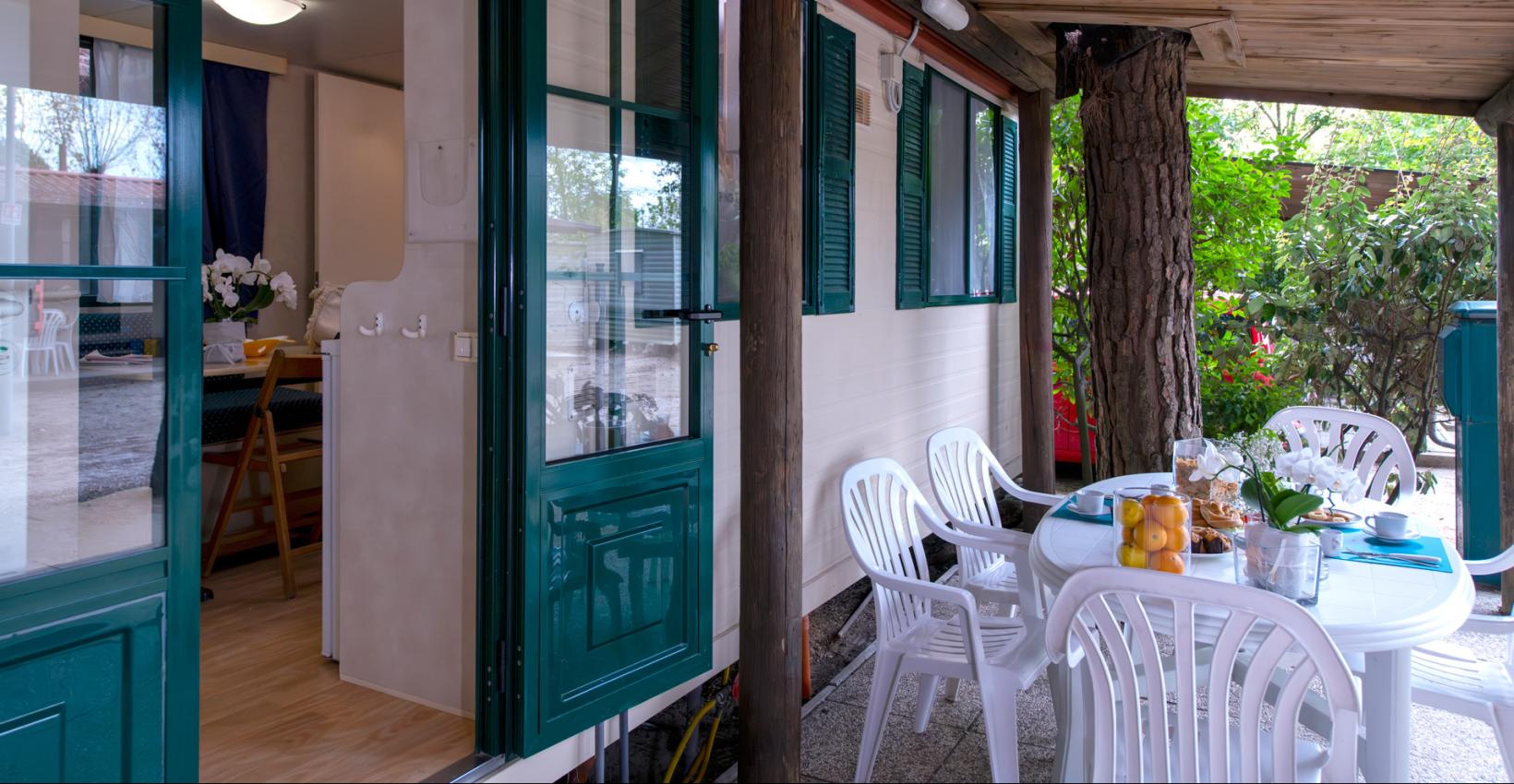 Veranda accogliente con tavolo imbandito, circondata da natura rigogliosa e atmosfera rilassante.