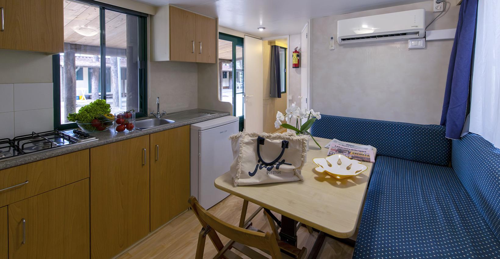 Interno accogliente con cucina compatta, divano blu, tavolo e atmosfera luminosa e rilassante.