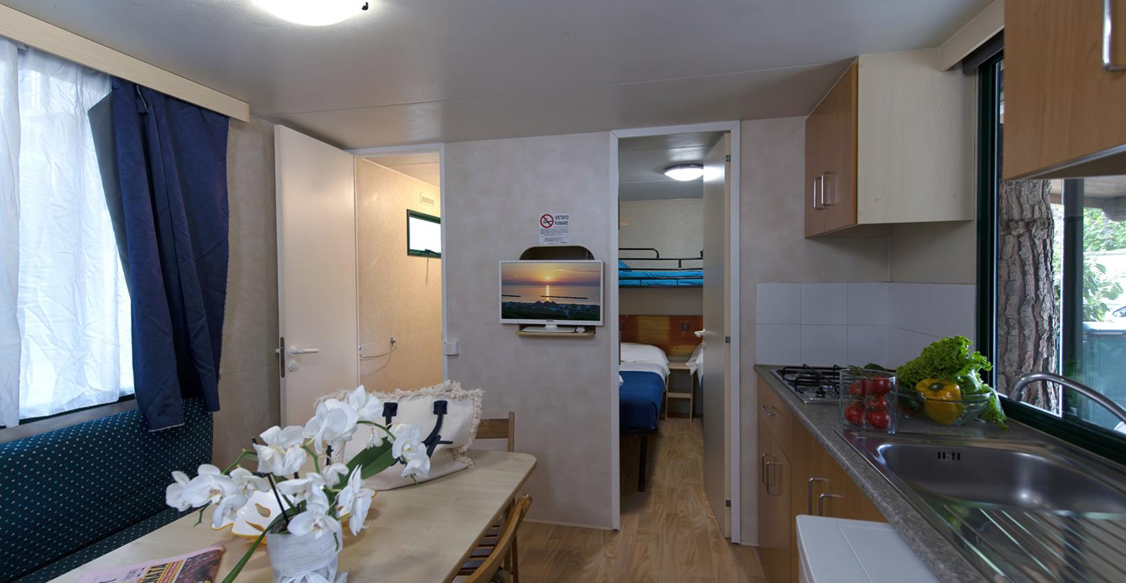 Accogliente casa mobile con cucina, tavolo fiorito e camera con letti a castello.